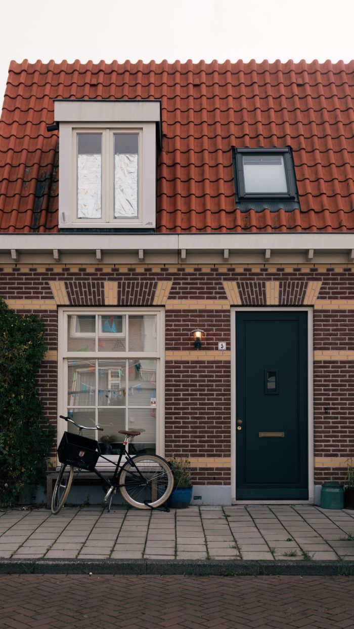 Cozy brick house facade with red roof and bicycle parked in Amsterdam.